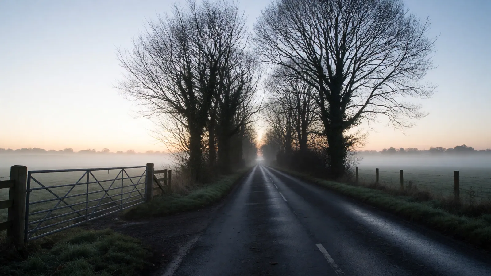 An empty road running out of the city at first light under a low grey sky, both lanes clear to the horizon